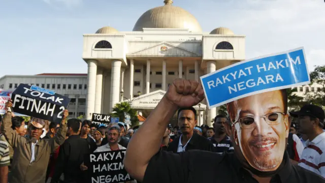 Người ủng hộ ông Anwar mang mặt nạ có hình ông trong lúc chờ tòa tuyên án tại Kuala Lumpur, thứ Hai, 09/01/2012. Dòng chữ trên có nghĩa: "Nhân dân là quan tòa của quốc gia".