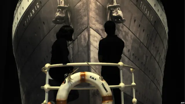 डूबे हुए जहाज़ का एक विशालकाय पोस्टर प्रदर्शनी स्थल के ठीक सामने लगा हुआ है जहां खड़े हैं दो दर्शक.