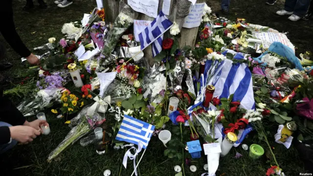 Bendera Yunani berdampur dengan karangan bunga.