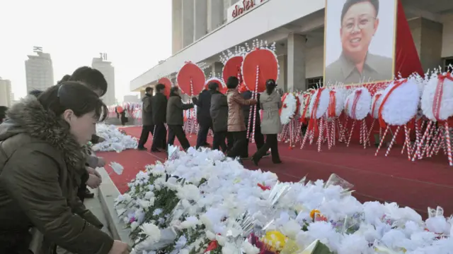 Tại các điểm công cộng, hình ông Kim Jong-il, tạ thế ở tuổi 69, được treo cao để người dân dâng hoa tập thể.