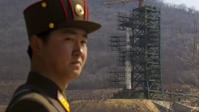 Một người lính Bắc Triều Tiên đứng trước hỏa tiễn Unha-3 đang được lắp vào bệ phóng.