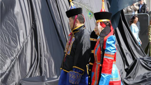 Люди в национальных костюмах у подножия памятника.