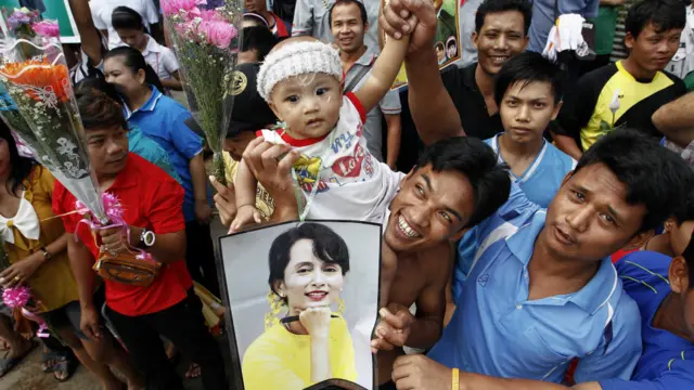 Miến Kiều ở Mahachai cầm ảnh chân dung của bà Suu Kyi để chào đón bà