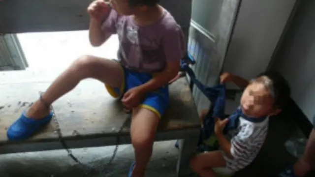 两名儿童被套上铁链及布条“拴养”。 (图片来自互联网)