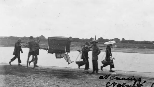 Носильщики несут мужчину в крытом палантине.