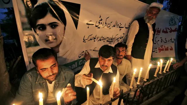 پشاور میں لوگ ملالہ یوسفزئی کے پوسٹر کے سامنے موم بتیاں جلا رہے ہیں