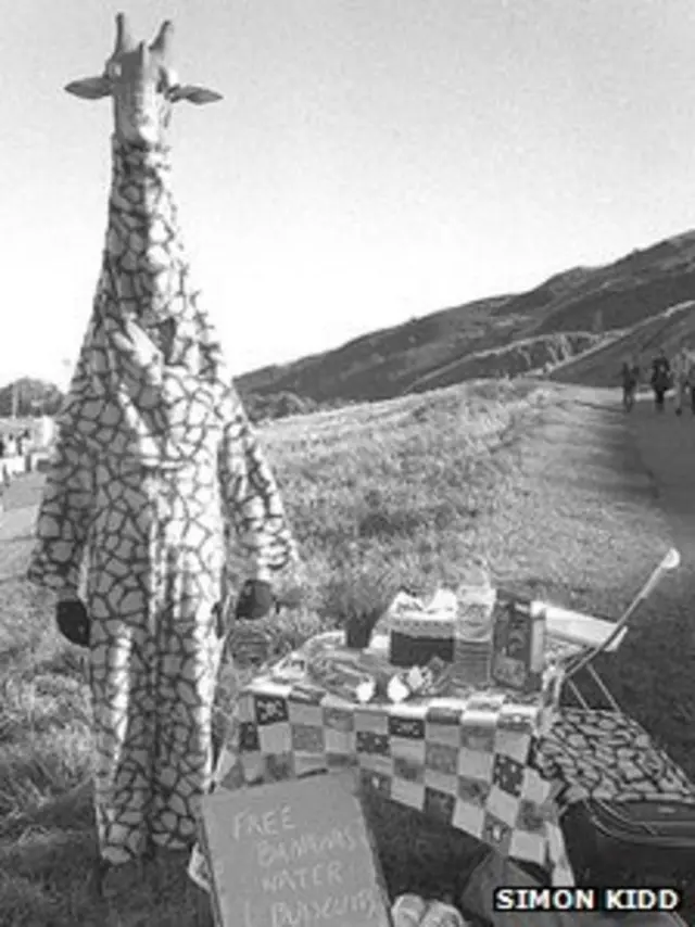 Armstrong Baillie vestido como jirafa repartiendo plátanos y agua.