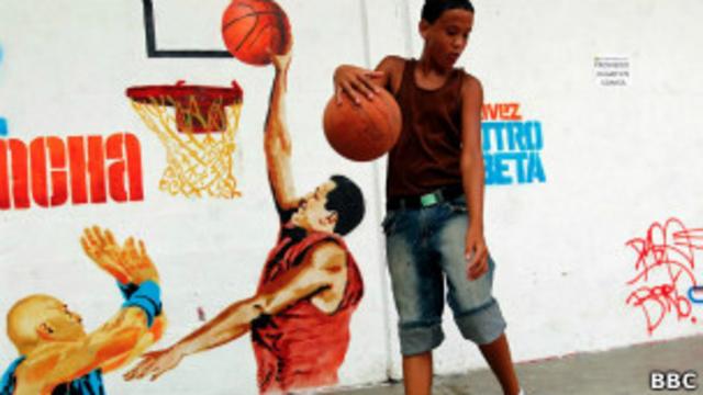 Menino brinca ao lado de grafite que mostra Chavez jogando basquete 