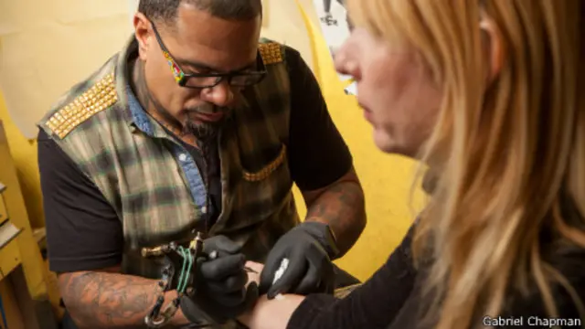 Tatuador comienza a grabar el logo de Rapid Realty en el antebrazo de una empleada