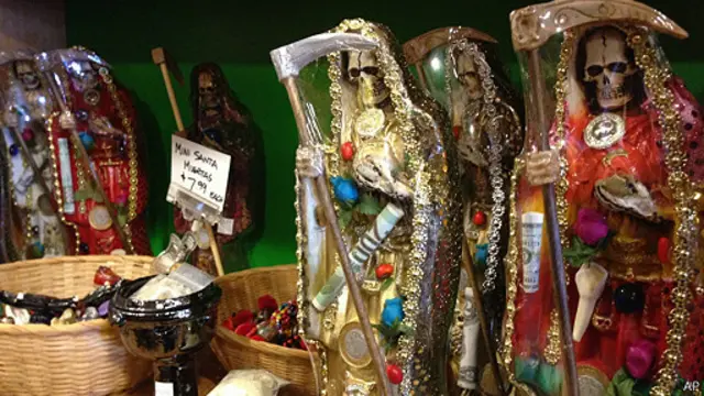 Farklı sembollerle tasvir edilmiş renkli Santa Muerte heykeli.