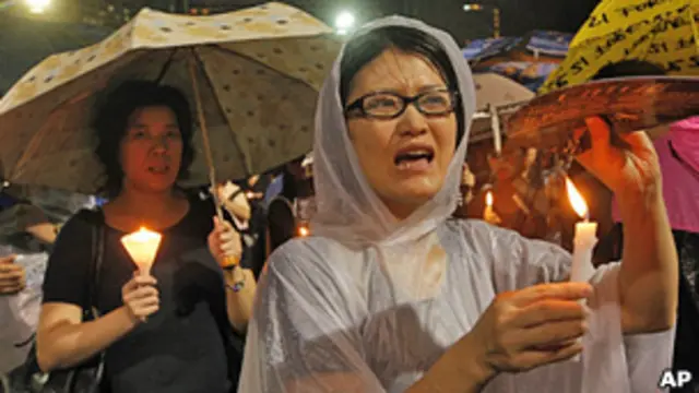 香港维多利亚公园六四烛光悼念晚会上一名穿上雨衣的女士高举烛光（4/6/2013）
