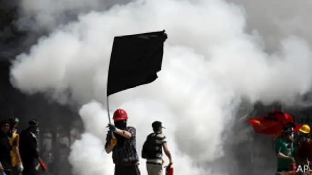 Протестующий с черным флагом перед баррикадой.