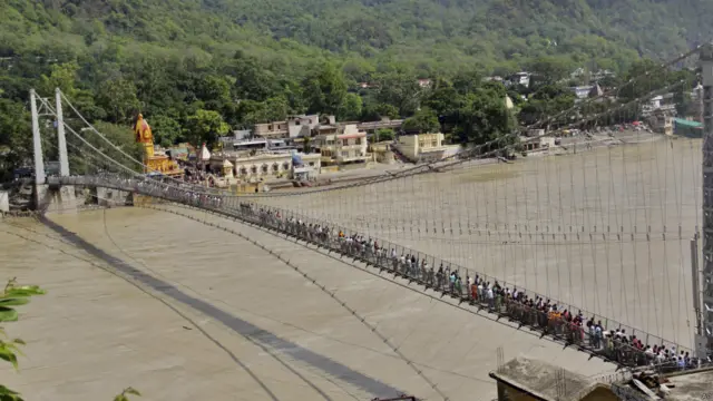 ऋषिकेश में उफनती गंगा के ऊपर लक्ष्मणझूला को पार करते लोग.