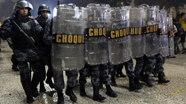 ريو دي جانيرو - كردوس من شرطة مكافحة الشغب يواجه المتظاهرين ليلة الخميس. أفادت تقارير بأن ما يقرب من 800 ألف شخص نزلوا إلى شوارع كبريات المدن البرازيلية الخميس للتظاهر احتجاجا على سياسات الحكومة. (أ.ف.ب.)