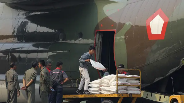 Para petugas menurunkan garam yang akan digunakan untuk membuat hujan buatan dari kapal kargo Angkatan Udara Sabtu (22 Juni). 