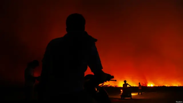 Penduduk desa dengan sepeda motor bersiap meninggalkan rumah-rumah mereka karena kebakaran yang melanda perkebunan sawit di Bangko Pusako.