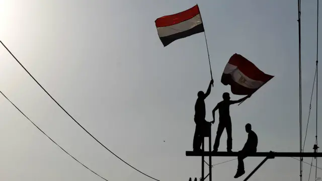 Manifestantes con banderas arriba de los postes, AFP
