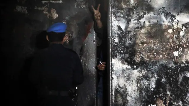 Seorang napi mengacungkan tanda perdamaian di balik pagar penjara, AFP