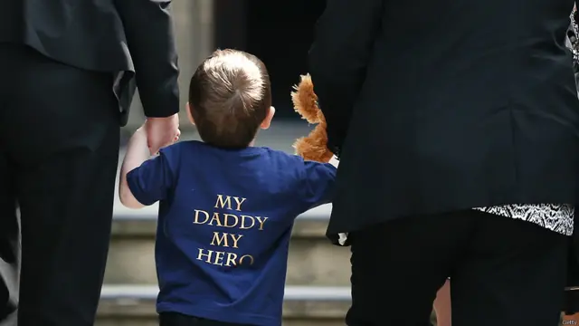 里格比的儿子在家人的带领下前往教堂，参加父亲的葬礼。他穿的T恤衫的背面写着：我的父亲，我的英雄。 