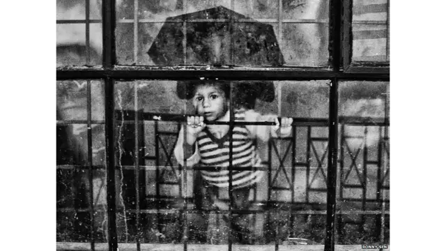 एक बच्चा राहत शिविर के गेट पर लगे कांच के दरवाजे से देखते हुए.