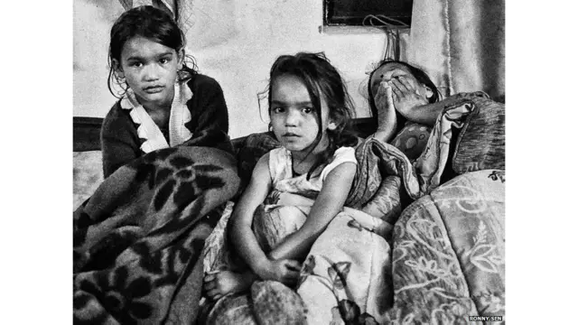 मंजू चौहान स्कूल जाने वाली अपनी दो पोतियों सुकन्या और संजना के साथ राहत शिविर में. उनकी मां मवेशियों की देखभाल के लिए बाढ़ प्रभावित गांव में ही हैं.