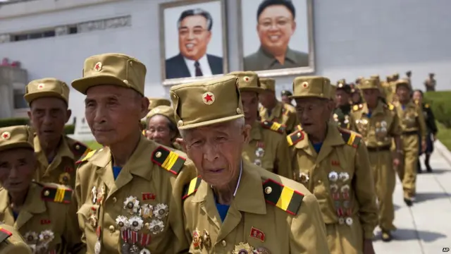 朝鲜老兵在阅兵式后走过悬挂已故领导人金日成（左）和金正日（右）画像的角落（27/7/2013）