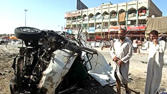 Civiles ante un auto destruido por una explosión en Irak