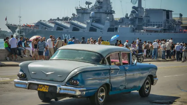 Un viejo auto estadounidense delante de uno de los buques