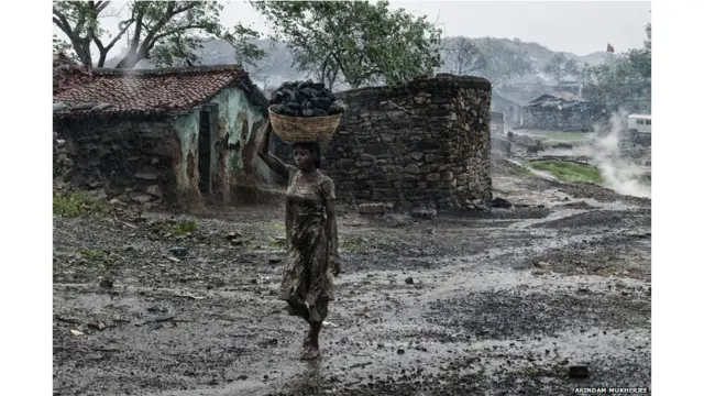 यहां रहनेवाले कई खनिक और उनके परिजन आग लगी खदानों से कुछ कोयला हासिल के करने की कोशिश में रहते हैं और फिर उसे ग़ैरक़ानूनी बाज़ार में बेचकर कुछ पैसे हासिल करने का प्रयास करते हैं. तस्वीर में एक युवती खुली खदान से बाल्टी में कोयला ले जाती नज़र आ रही है. 