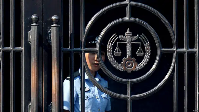 一名女警察在济南中院办公大楼的门后向外窥探，明天的庭审不知被告人还会爆出什么惊人的言语。