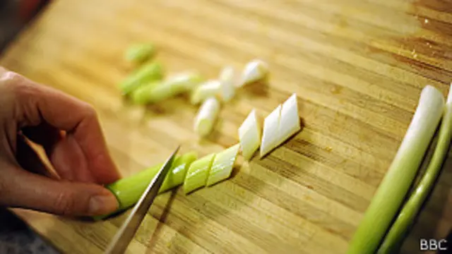 Alguien corta cebolla sobre una tabla de madera