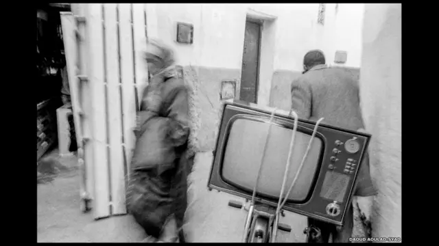 اما المراكشي داود ولد سيد، المتأثر بالمصورين هنري كارتييه بريسو وروبرت فرانك وريتشارد افيدون، فقد تخصص بتصوير الرحلات المنفردة التي قام بها في ارجاء المغرب. في هذه الصورة، ينقل رجل جهاز تلفاز في الرباط.