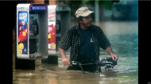  En esta foto, tomada el domingo en Acapulco un hombre trata de desplazarse por la ciudad junto a su bicicleta. 