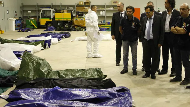 Yetkililer, İtalya kıyılarına varmaya çalışan Afrikalı göçmenlerin Lampedusa havaalanı hangarındaki ceset torbalarını inceliyor.