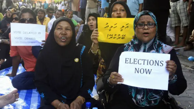 Женщины с плакатами сидят на дороге в Мале