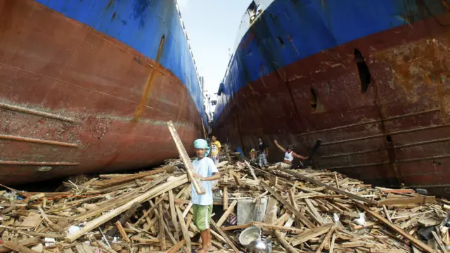 Tayfunun ardından kıyıda biriken keresteleri toplayarak yeniden kullanmaya çalışan insanlar.