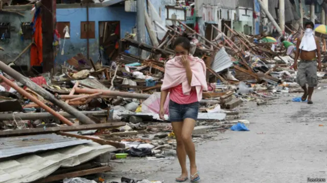 ساکنان تاکلوبان در مرکز فیلی‌پین که با صورت‌های پوشیده در میان ویرانی‌ها قدم می زنند. توفان هایان که جان بیش از ده هزار نفر را گرفت هشتصد کیلومتر عرض داشت.