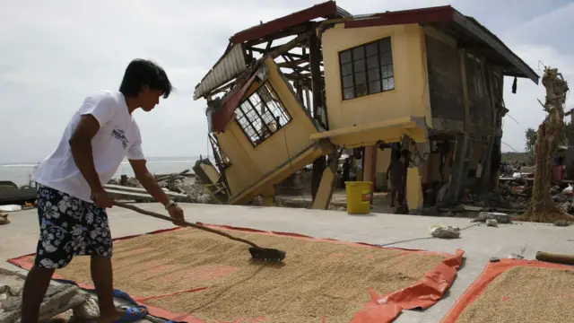 Yıkılan evinin önünde ıslanan pirinç stokunu kurutan bu Filipinli de yaşama yeniden tutunmaya çalışan milyonlardan biri.