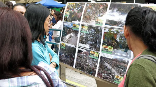 菲律宾家佣在香港遮打道路旁一处工会筹款摊位观看灾区的新闻照片（17/11/2013）