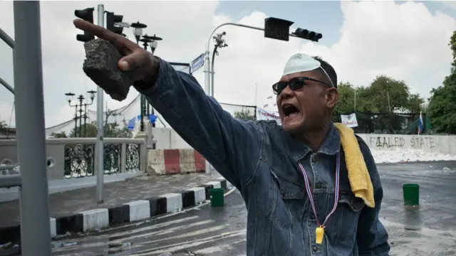 ایک شخص ہاتھ میں پتھر اٹھائے سکیورٹی فورسز کی جانب اشارہ کر رہا ہے۔