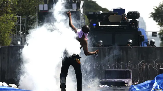 बैंकाक की एक इमारत में आंसू गैस के गोले को वापस फेंकता एक प्रदर्शनकारी