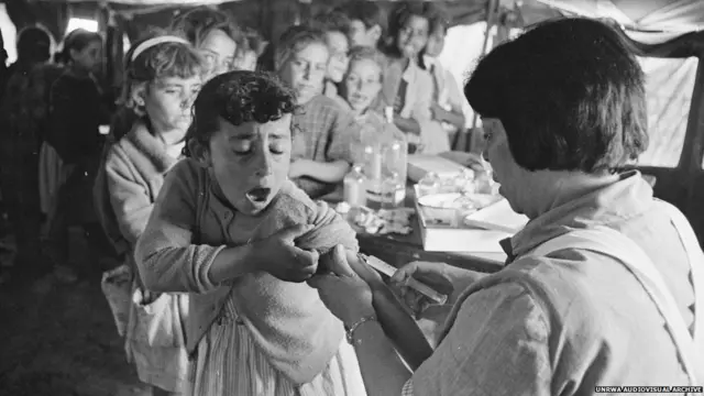 انتشار الأمراض نظراً للازدحام في المخيمات كان من المشاكل التي واجهت تلك المخيمات في أيامها الأولى. الصورة لطفلة يتم تطعيمها ضد الكوليرا في مخيم بالأردن عام 1971.