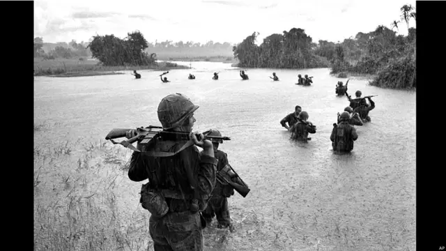 ویت کونگ کی تلاش میں امریکی فوجی ہتھیاروں کو سر سے اوپر کیے دریا عبور کرتے ہوئے۔