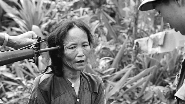 ایک عورت جس پر شک ہے کہ وہ ویت کونگ کی مخبر ہے۔ اس کی کنپٹی پر بندوق رکھ کر اس سے تفتیش کی جا رہی ہے۔ 