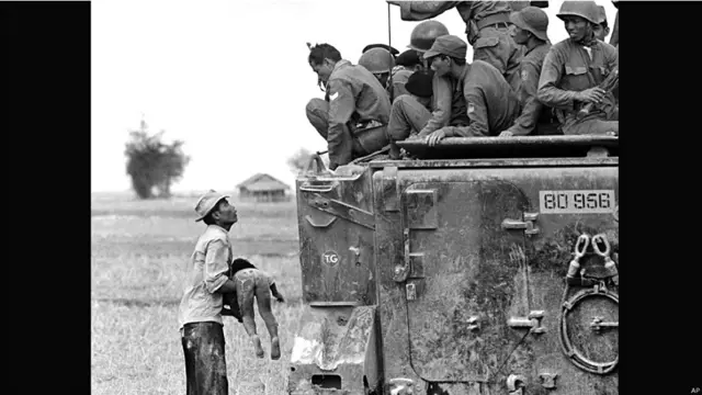 ایک شخص نے اپنے مردہ بچے کو اٹھا رکھا ہے جب کہ جنوبی ویتنامی فوجی دیکھ رہے ہیں۔ 