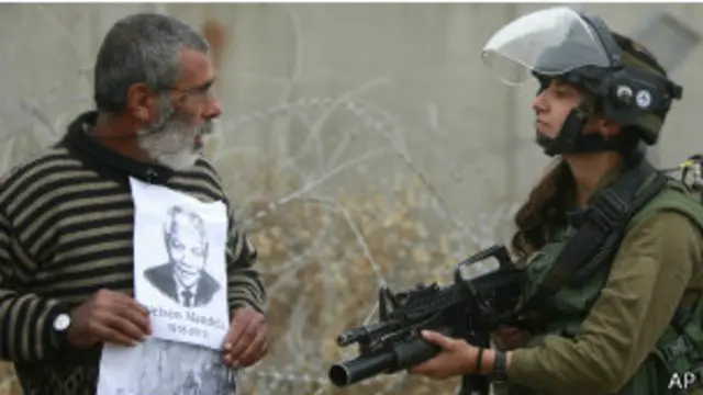 جندية إسرائيلية تصوب بندقيتها تجاه متظاهر يحمل صورة مانديلا