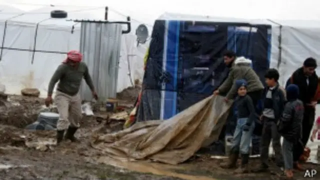 لاجئون يحاولون حماية خيمهم من الأمطار