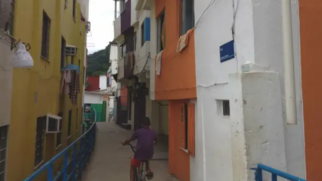 A subida revela vielas mais estreitas, muitas com esgoto a céu aberto. Cinco anos após receber a primeira UPP do Rio, a Santa Marta ainda não tem saneamento básico  Já na metade do morro, a  maioria das casas recebeu pintura nova e muitas das vielas estão identificadas. (Foto: Jefferson Puff/BBC).
