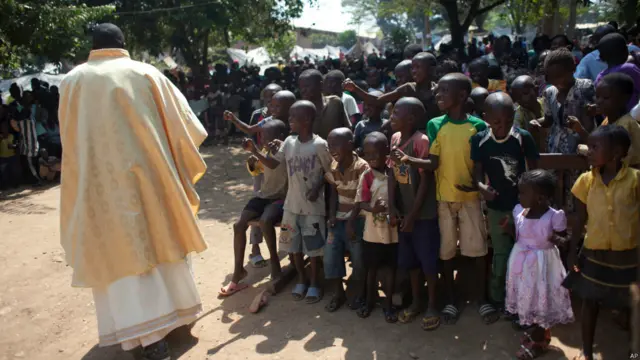 أطفال يتفاعلون من رئيس الأساقفة خلال حفل عيد الميلاد في ساحة تعد معسكرا للمشردين في مدينة بانغوي بجمهورية إفريقيا الوسطى