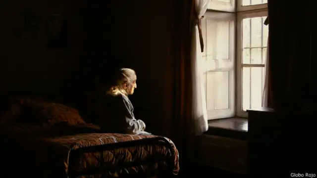 Anciana sentada en una cama mirando a la ventana